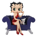A collectible figurine of classic cartoon character Betty Boop sitting on a small tufted purple sofa with a white dog, photographed against a solid white background.