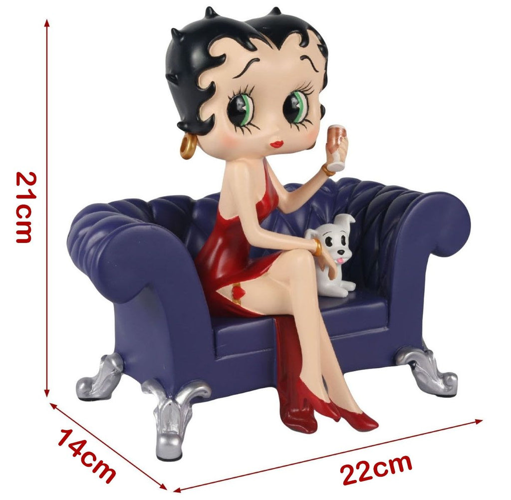 A Betty Boop figurine sitting on a small tufted blue sofa with a white dog, shown with red dimension arrows and labels indicating 21 cm height, 14 cm width, and 22 cm depth on a white background.